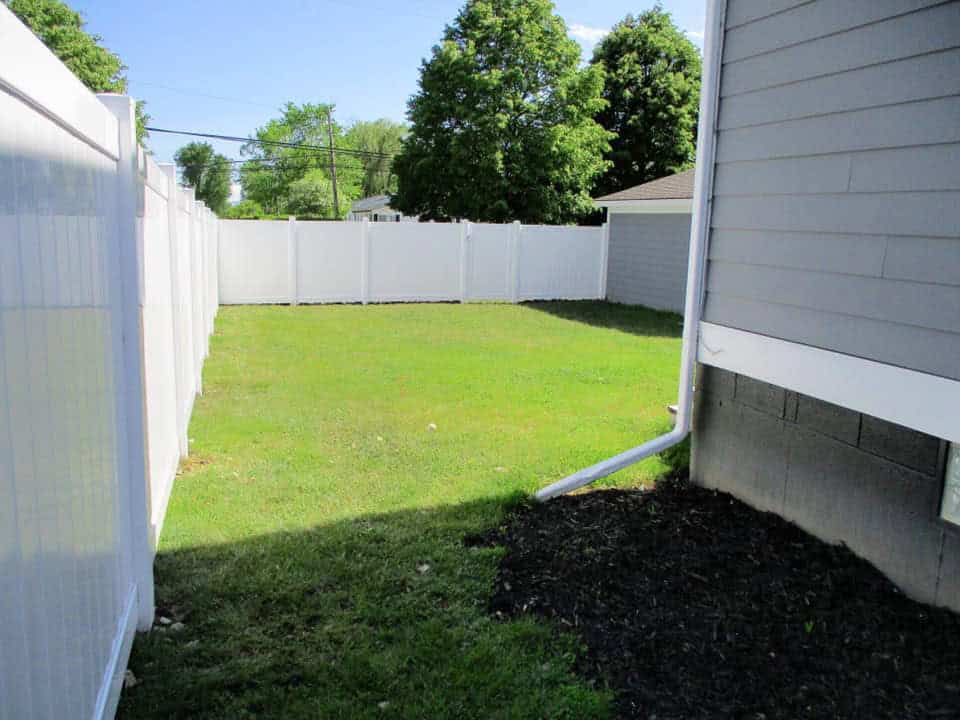 Fenced backyard with green grass and trees.