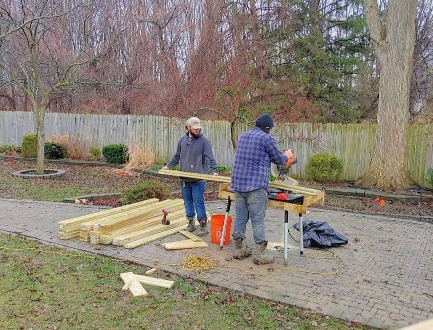 Two men building wooden structure outdoors.